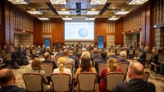 widok na salę konferencyjną z publicznością, scenę, mównicę i ekran z prezentacją