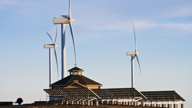 Turbiny wiatrowe i farma fotowoltaiczna obok budynku na otwartej przestrzeni.