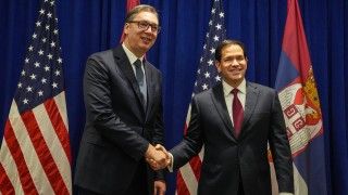 Prezydent Serbii Aleksandar Vuczić ściska dłoń sekretarza stanu USA Marco Rubio na tle serbskich i amerykańskich flag.