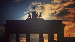 brama brandenburska o wschodzie słońca, brama jest ciemna, słońce za nią