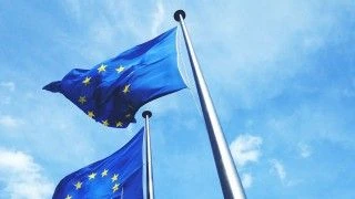 Dwie flagi Unii Europejskiej powiewające na tle błękitnego nieba.