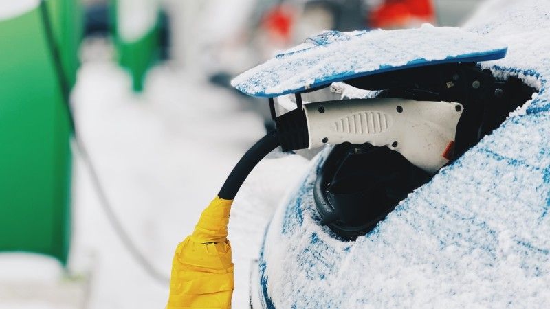 Samochód elektryczny podłączony do ładowania zimą.