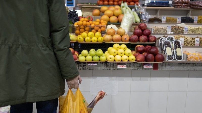 Mężczyzna z torbą z zakupami stoi przed kasą w sklepie spożywczym.