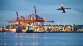 Widok na port morski z poziomu morza, światła w oddali i odlatujący samolot.