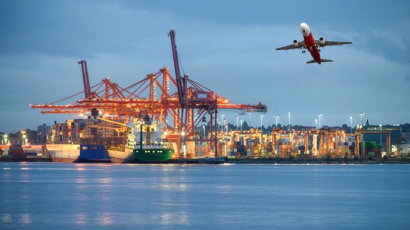 Widok na port morski z poziomu morza, światła w oddali i odlatujący samolot.