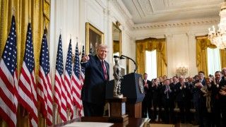 Prezydent USA Donald Trump przemawiający na tle licznych amerykańskich flag.