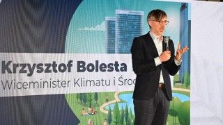 Wiceminister stoi na tle banneru z napisem: Krzysztof Bolesta Wiceminister klimatu i środowiska, mówi do mikrofonu