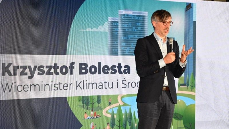 Wiceminister stoi na tle banneru z napisem: Krzysztof Bolesta Wiceminister klimatu i środowiska, mówi do mikrofonu