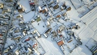 Widok z lotu ptaka na budynki mieszkalne i pola przysypane śniegiem.