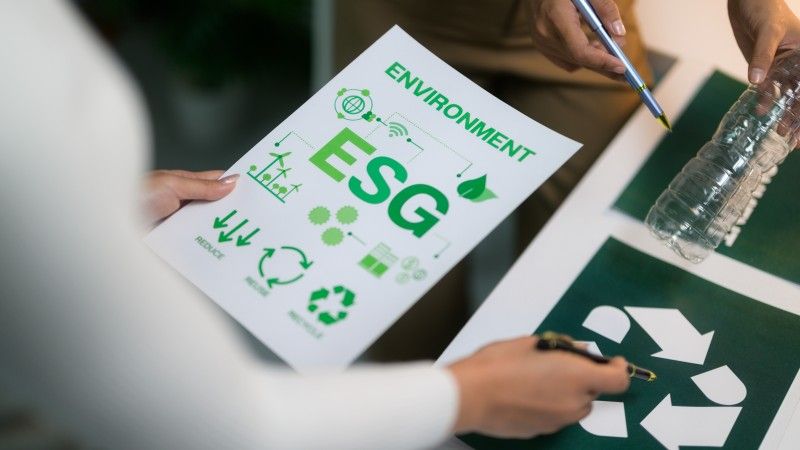 ludzie trzymają kartkę a napisem ESG, pustą plastikową butelkę, wskazują sobie fragmenty długopisami, nie widać twarzy