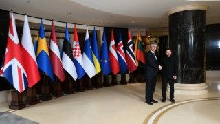 Mężczyźni ściskają sobie dłonie na tle flag państw UE, Ukrainy i UE