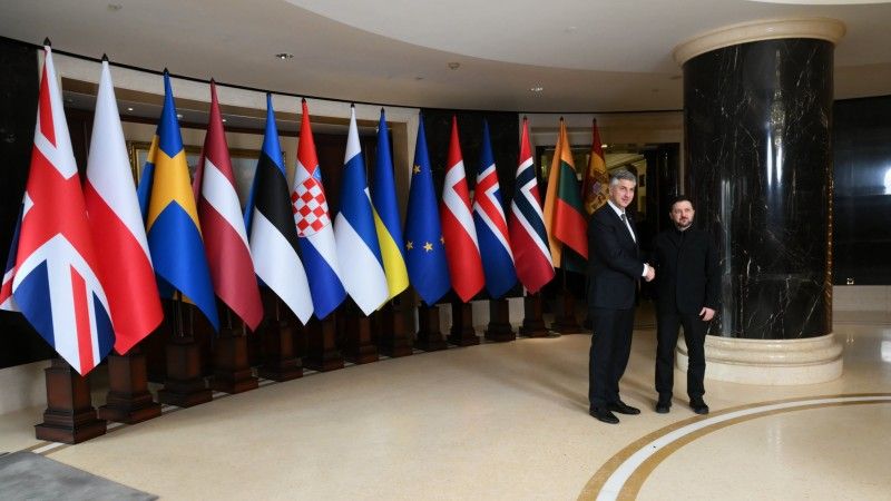 Mężczyźni ściskają sobie dłonie na tle flag państw UE, Ukrainy i UE