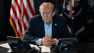 Donald Trump za biurkiem, przy monitorach