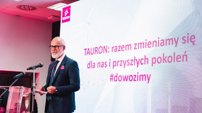 Prezes przemawia zza mównicy na tle prezentacji