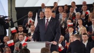 Czarnek stoi za mównicą, za nim na trybunach siedzą osoby z flagami Polski w rękach