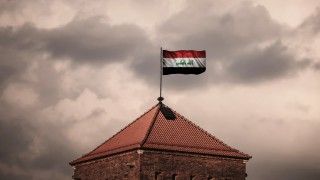 flaga Iraku powiewa na szczycie wieży na tle zachmurzonego nieba