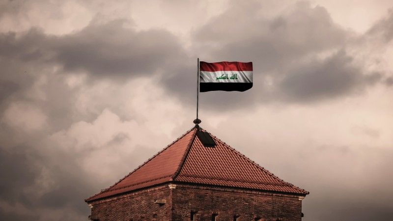 flaga Iraku powiewa na szczycie wieży na tle zachmurzonego nieba