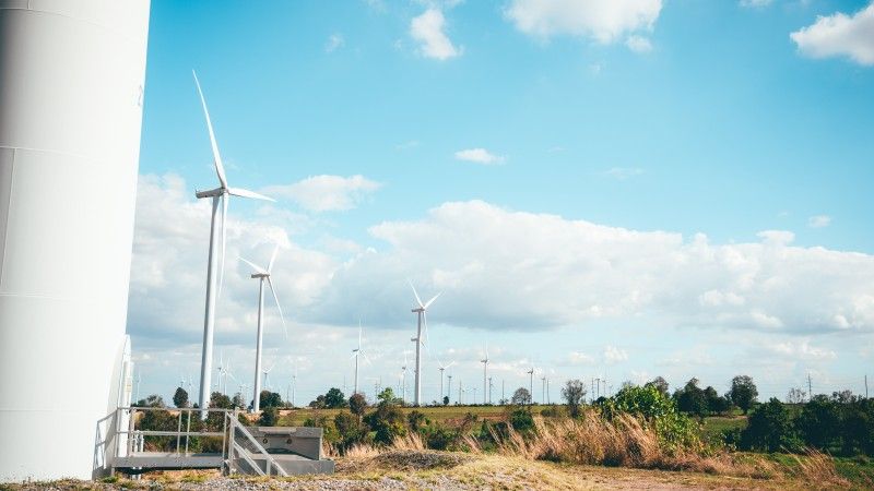 turbiny wiatrowe na lądzie, pierwsza jest blisko na pierwszym planie, widać drzwi, reszta daleko w tle