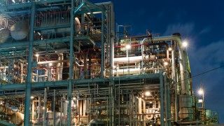 widok na fragment fabryki chemicznej w nocy, widać dużo rur i zbiorników