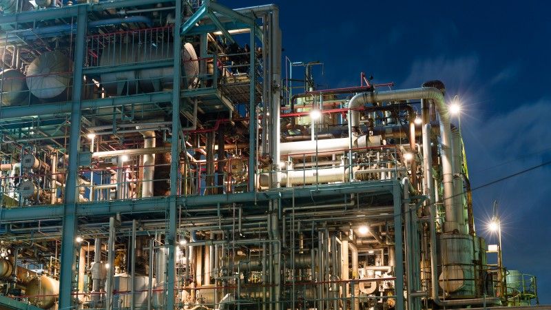 widok na fragment fabryki chemicznej w nocy, widać dużo rur i zbiorników