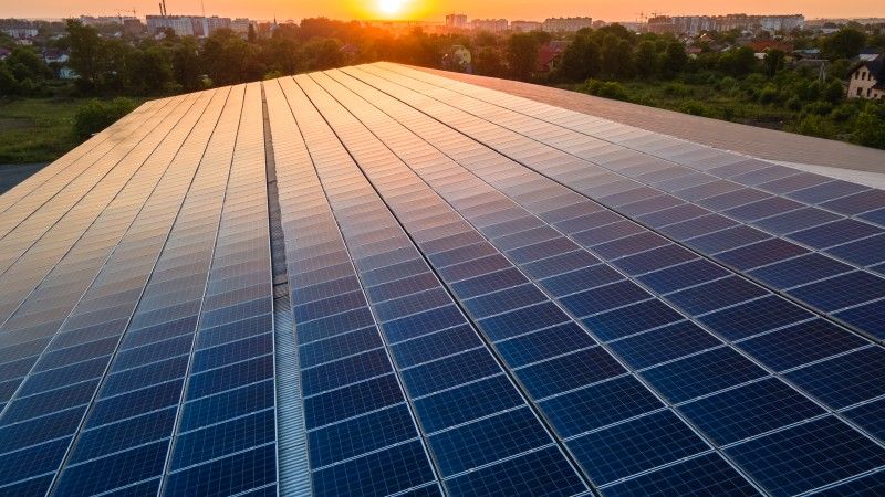 słońce zachodzące nad panelami fotowoltaicznymi zainstalowanymi na dachu, w tle miasto