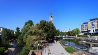 Ulica w mieście Pforzheim w południowo-zachodnich Niemczech z widokiem na wieżę kościoła, rzekę, drzewa i nowoczesny budynek.