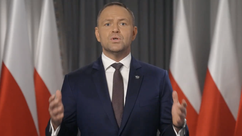 Karol Nawrocki przemawia na tle flag Polski