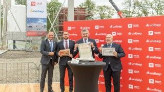 Prezesi i władze lokalne trzymają podpisany akt budowy kapsuły czasu na tle ścianki Unibep i Orlen Termika