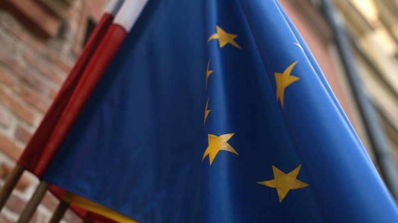 Flaga Unii Europejskiej na budynku, w tle flaga biało-czerwona.