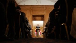 premier przemawia zza mównicy na tle flag Wielkiej Brytanii