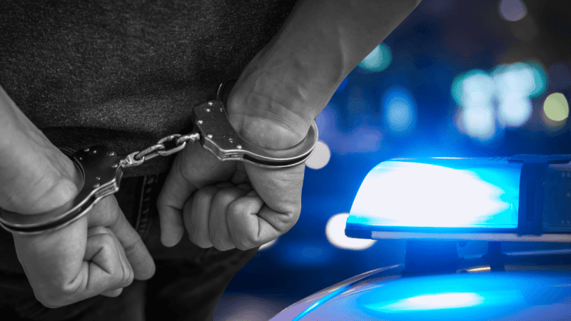 Dłonie hakera w kajdankach prowadzonego przez policję. Historyczna akcja Interpolu i rozbicie sieci oszustów w 13 krajach.