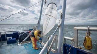 mężczyzna w kombinezonie jest na tyle statku, pobiera próbkę wody z dużego urządzenia
