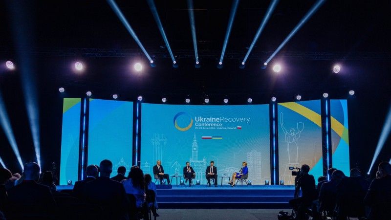 Paneliści na scenie podczas konferencji, z oddali, w tle logo Ukraine Recovery Conference
