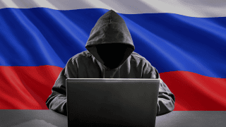 Hacker przed komputerem na tle rosyjskiej flagi.
