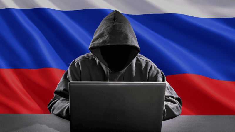 Hacker przed komputerem na tle rosyjskiej flagi.