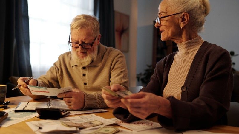 para seniorów przy stole liczy rachunki i banknoty przy użyciu kalkulatora