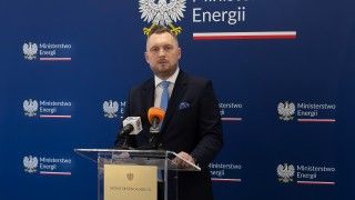 Minister stoi za mównicą, przemawia na tle ścianki ministerstwa energii