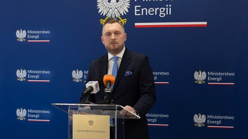 Minister stoi za mównicą, przemawia na tle ścianki ministerstwa energii