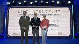 osoby stoją na scenie na tle podpisanego listu intencyjnego