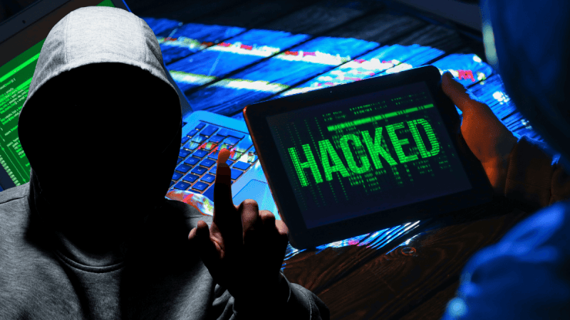 Hackerzy z tabletem i napisem na ekranie "HACKED".