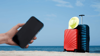 Walizki na plaży i smartfon w ręku.