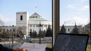 Budynek Sejmu RP w Warszawie widziany zza okna, na pierwszym planie dokument dotyczący ustawy o systemach sztucznej inteligencji oraz ekran komputera.