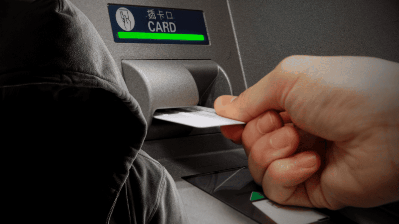 Bankomat, karta bankowa oraz mężczyzna w kapturze.