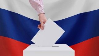 Mężczyzna wrzuca kartę do urny na tle rosyjskiej flagi - zdjęcie ilustracyjne