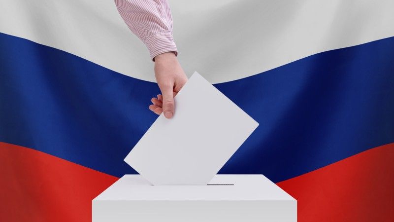 Mężczyzna wrzuca kartę do urny na tle rosyjskiej flagi - zdjęcie ilustracyjne