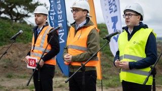 ministrowie w ubiorze ochronnym na placu budowy przemawiają do mikrofonów