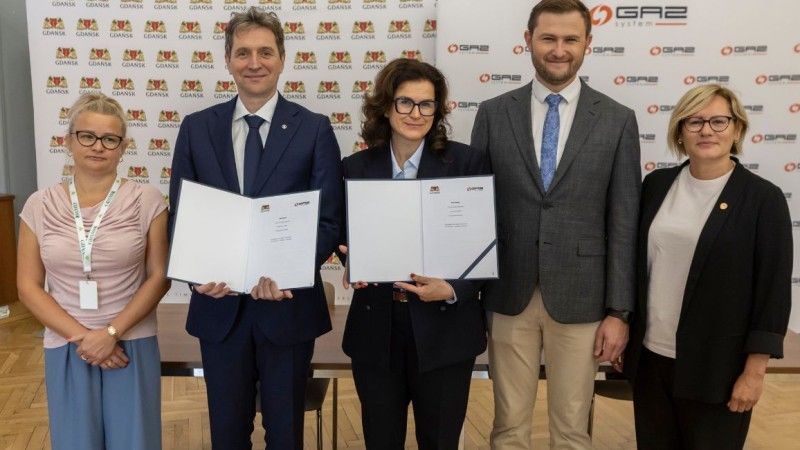 przedstawiciele stoją z podpisaną umową na tle ścianek spółki i miasta