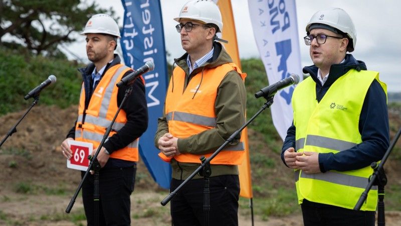 ministrowie w ubiorze ochronnym na placu budowy przemawiają do mikrofonów