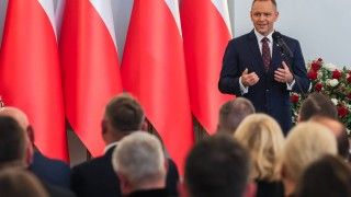 Karol Nawrocki przemawia do mikrofonu na tle flag RP