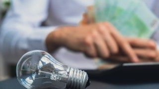 osoba oblicza rachunek za energię, na stole leży żarówka